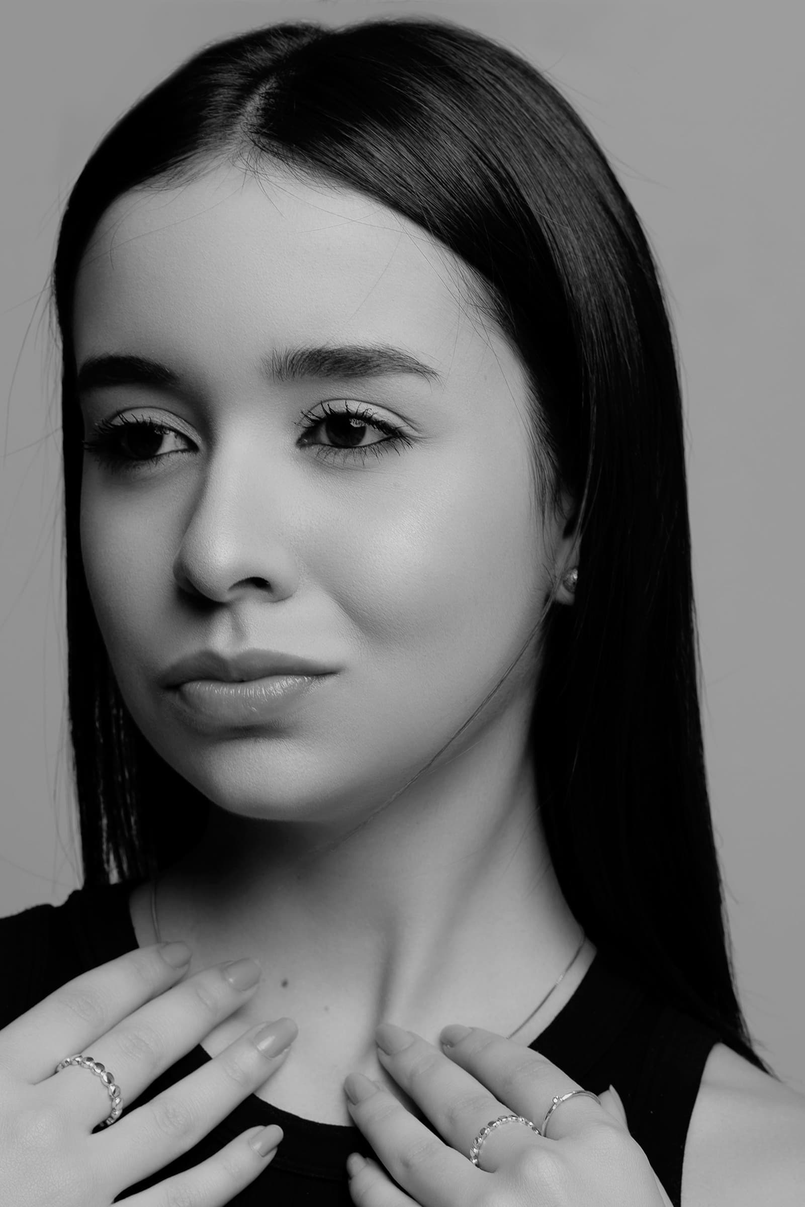 Foto de uma jovem mulher com pele clara e cabelos longos, olhar suave e cabelo liso escuro, em uma foto em preto e branco, transmitindo elegância e beleza natural.