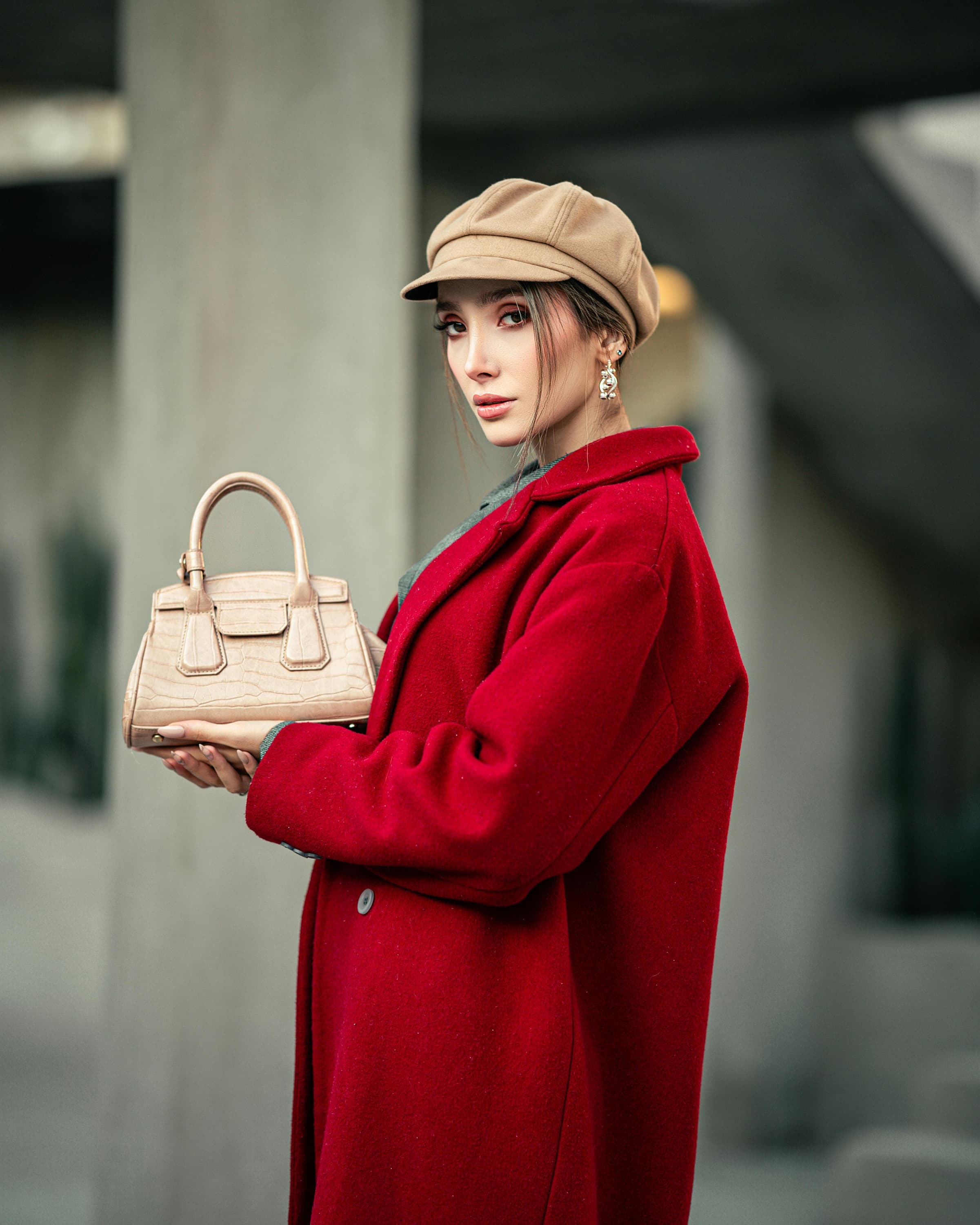 Foto de uma mulher estilosa com blazer vermelho, chapéu bege e bolsa de mão, posando ao ar livre em ambiente urbano na cidade de dia.