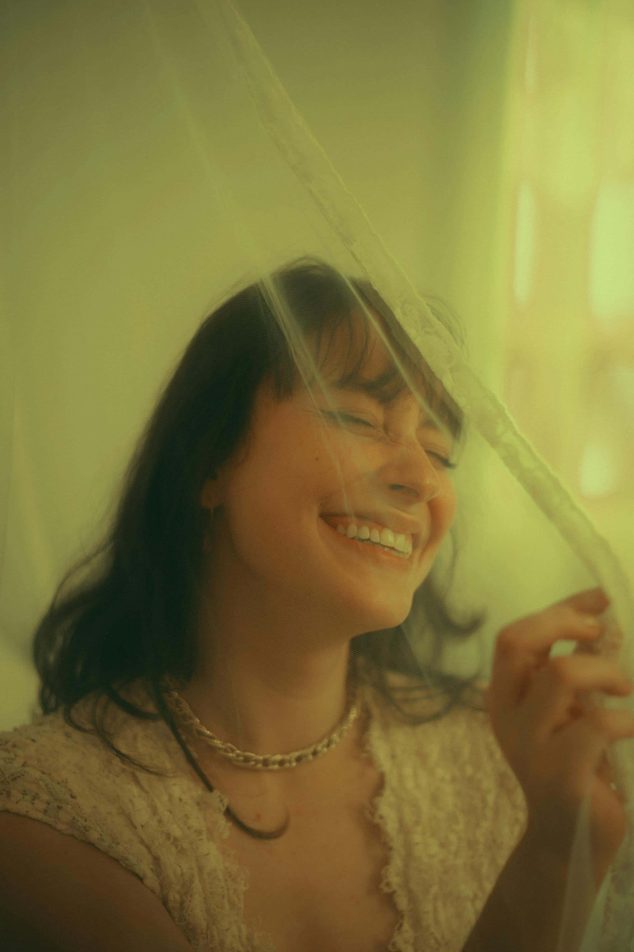 Foto de uma mulher com cabelo escuro sorrindo usando um colar, com iluminação quente, estilo vintage e com efeito desfocado.