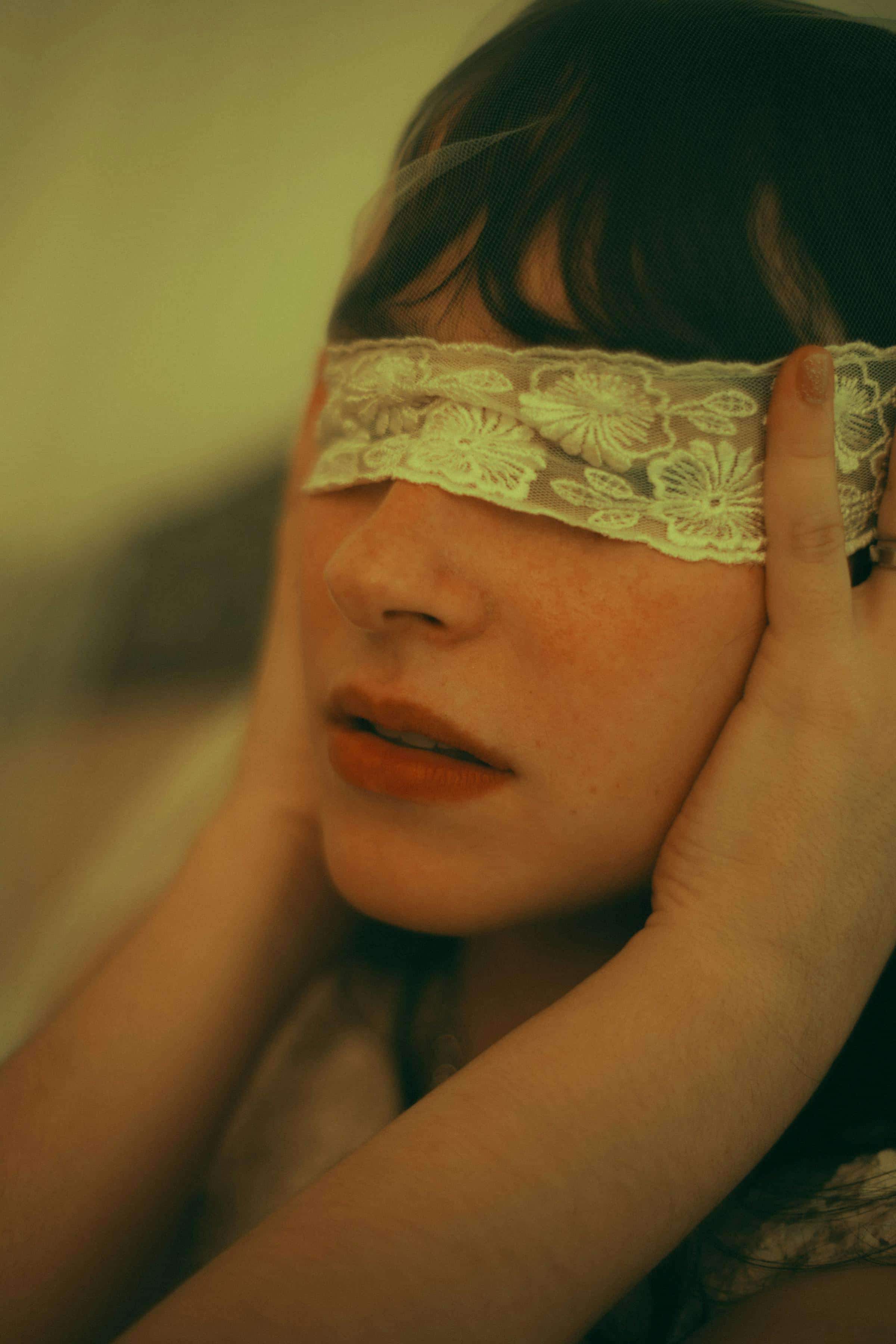 Foto de uma mulher com cabelo escuro usando uma faixa de renda floral sobre os olhos, com iluminação quente, estilo vintage.